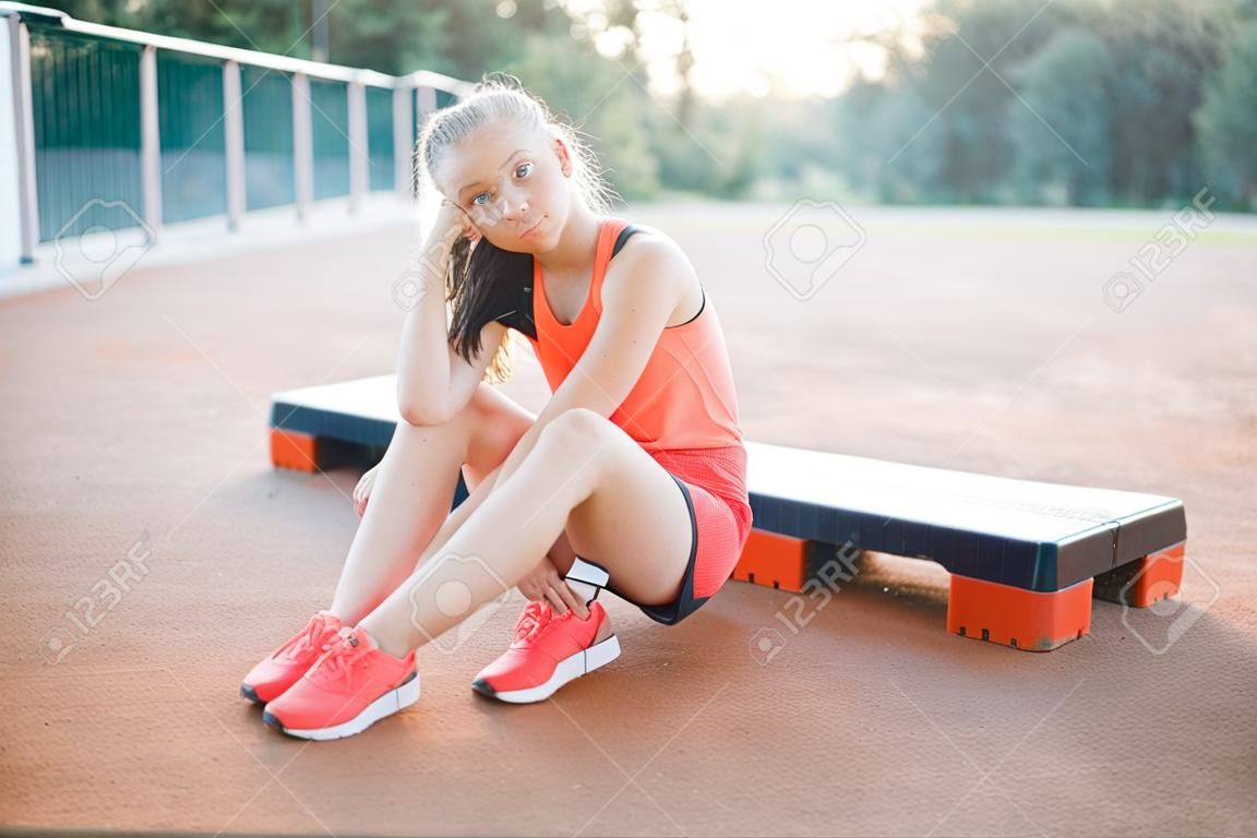 Een schattig, mooi tienermeisje zit op een step platform en ontspant zich na haar training op outdoor