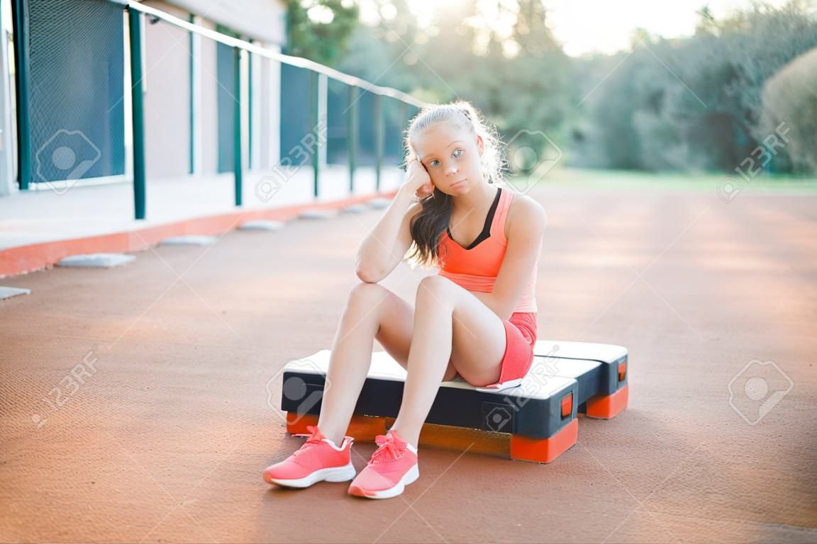 Een schattig, mooi tienermeisje zit op een step platform en ontspant zich na haar training op outdoor