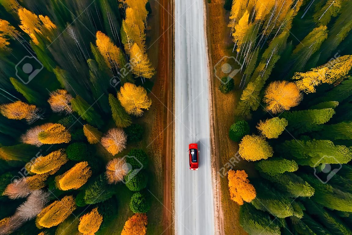 Luftaufnahme der Landstraße mit rotem Auto im gelben und orangefarbenen Herbstwald im ländlichen Finnland.