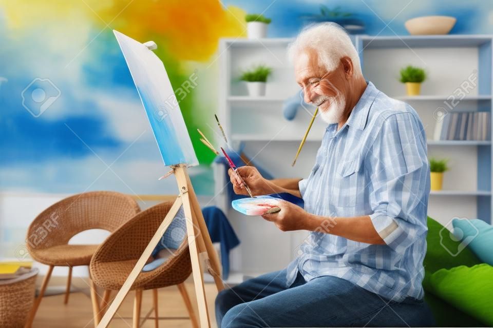 Szczęśliwy emeryt malujący na płótnie dla zabawy w domu