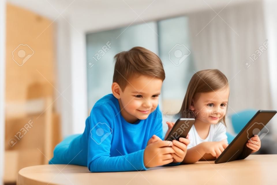 어린 소녀와 소년이 디지털 장치 태블릿, 스마트폰으로 비디오를 보거나 게임을 합니다.