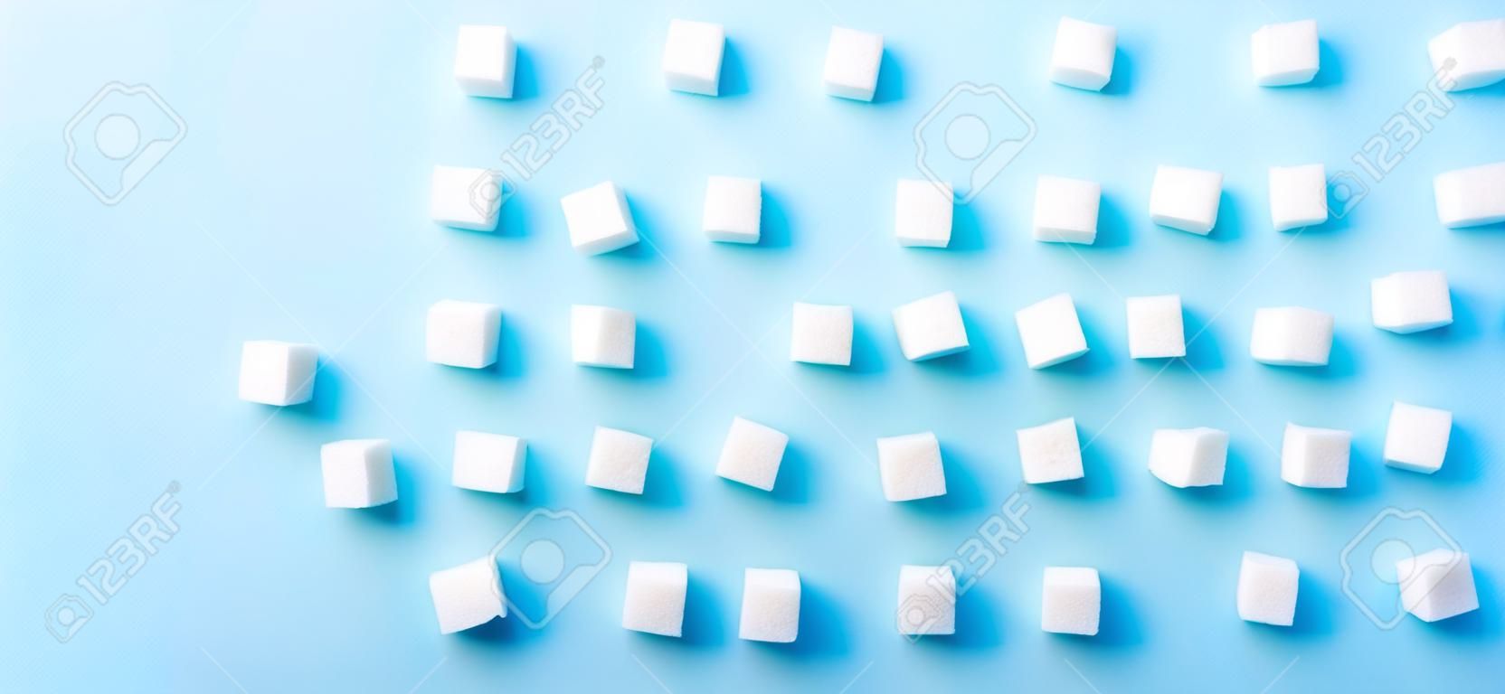 Sugar cubes regular pattern on blue background, flat lay banner with copy space