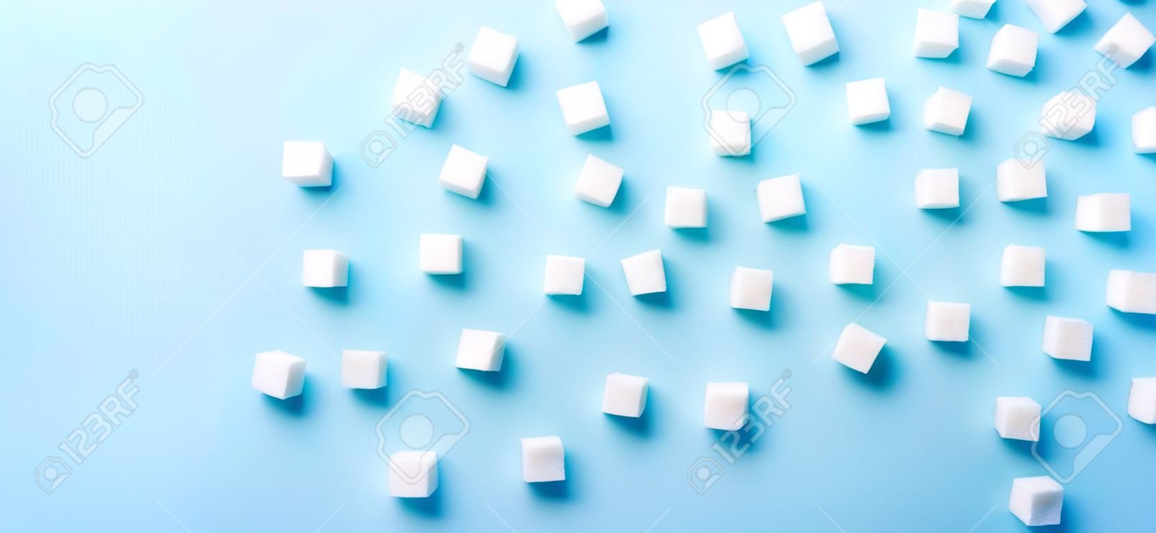 Sugar cubes regular pattern on blue background, flat lay banner with copy space