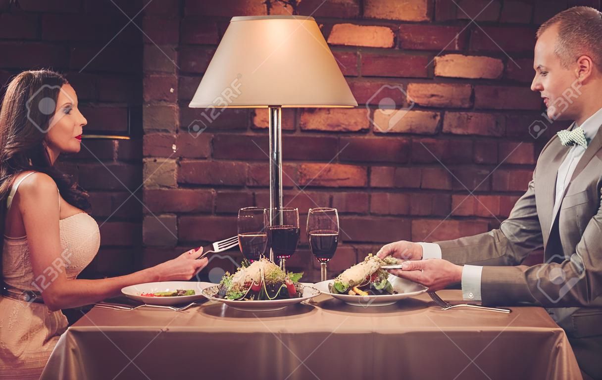 Waiter serving a plate of salad to stylish wealthy couple in a restaurant.