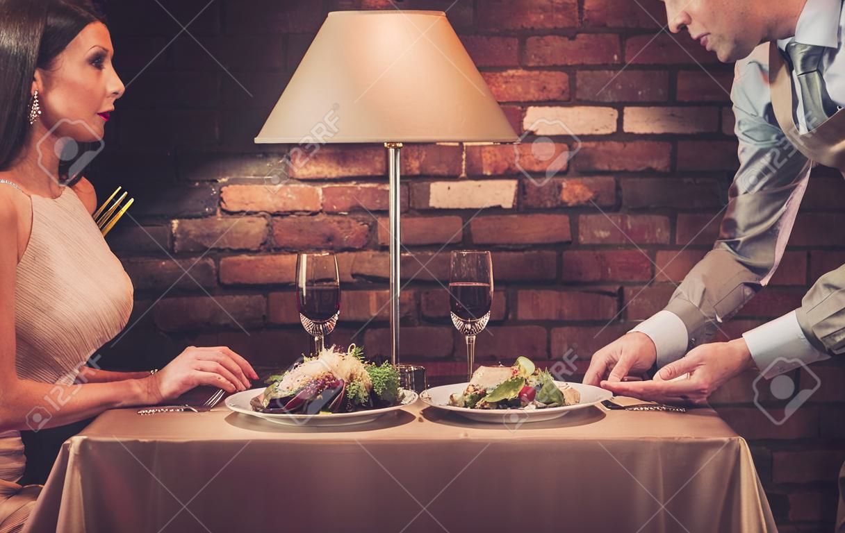 Camarero que sirve un plato de ensalada de pareja rica elegante en un restaurante.