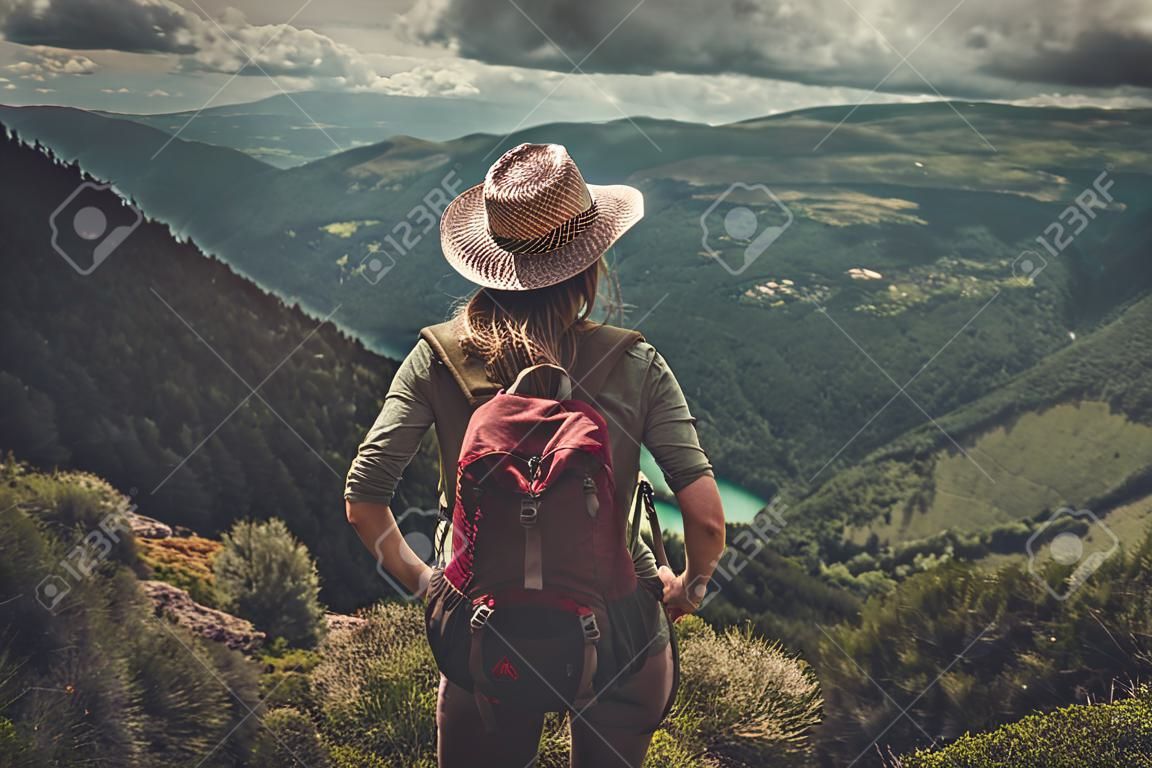 Woman hiker with backpack enjoying amazing valley landscapes on a top of mountain.