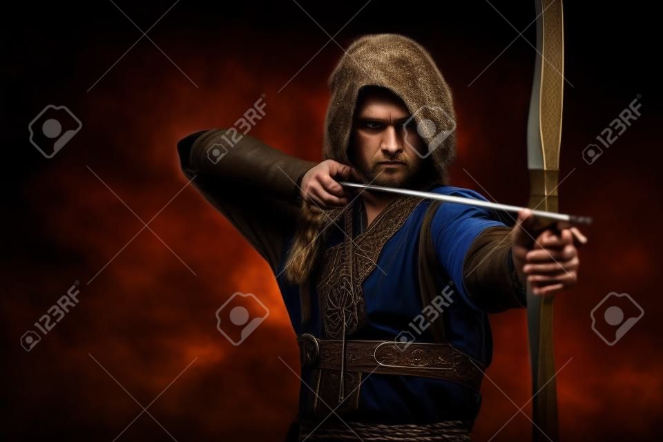 viking serio con l'arco e la freccia in un tradizionale abito guerriero, posa su uno sfondo scuro.