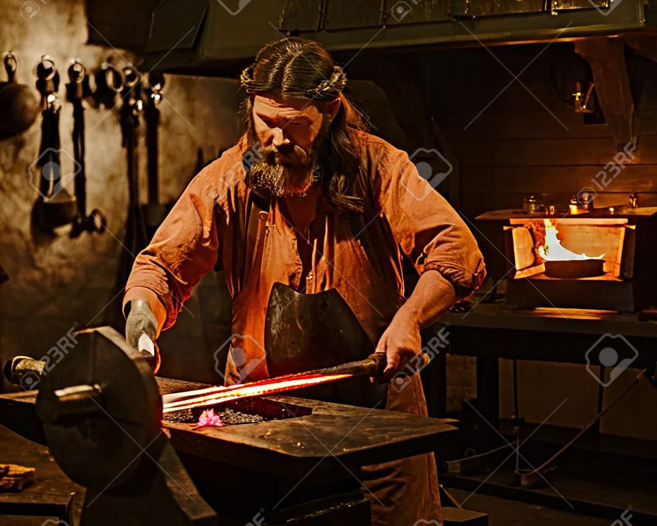 Senior blacksmith forging the molten metal on the anvil in smithy.