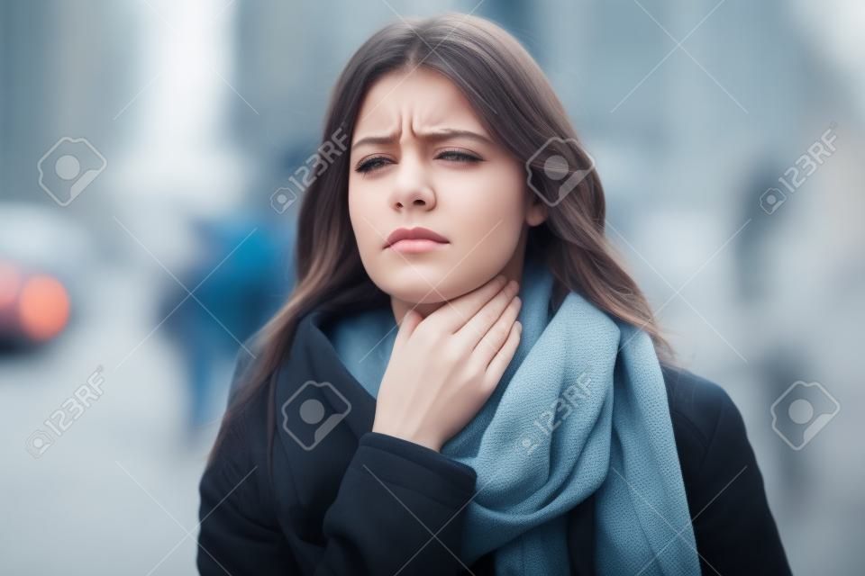 Aufnahme einer jungen Frau mit schrecklichen Halsschmerzen, die auf die Straße geht.