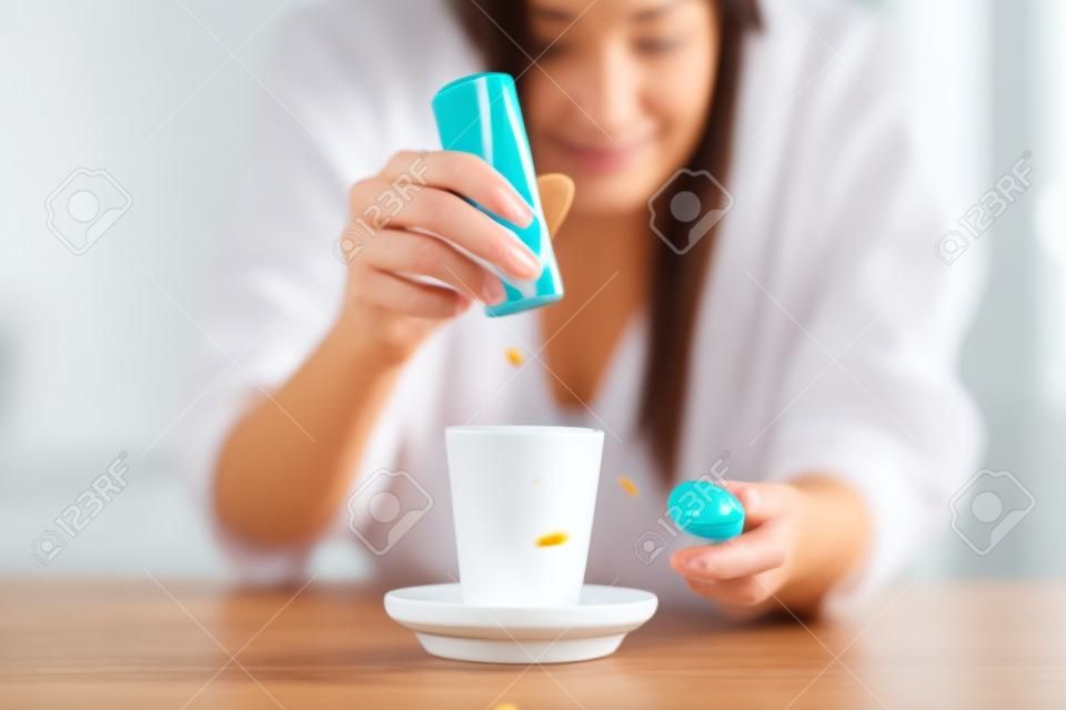 Close-up da mão da mulher jogando pílulas de sacarina no copo de café na cozinha em casa.