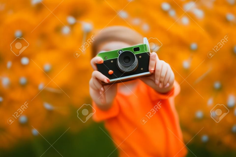 Young beautiful girl in an orange T-shirt holding retro camera in her hands lying on the lawn where dandelions grow, flowering dandelions