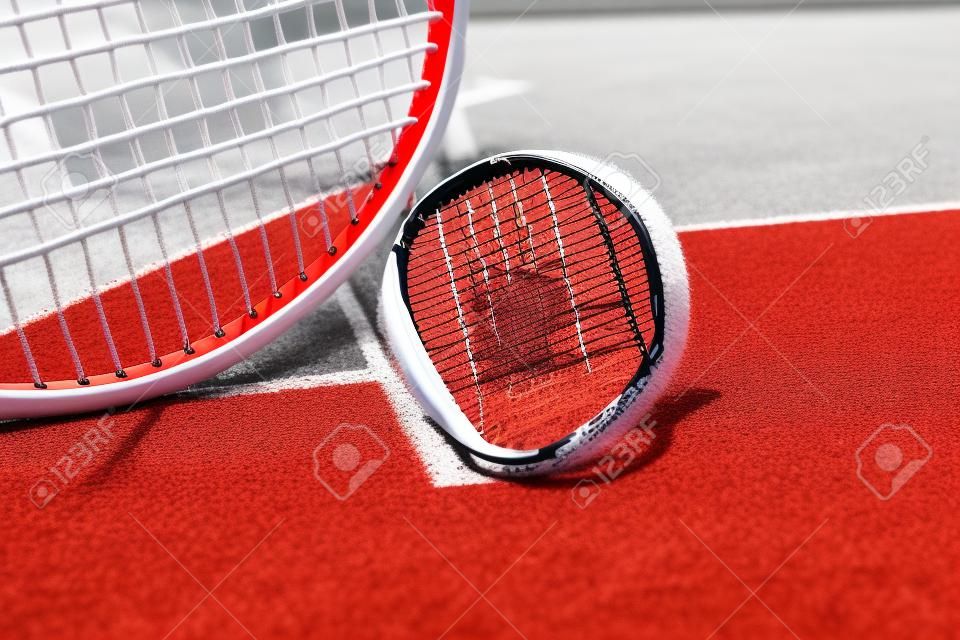 빨간색 하드 코트 표면에 흰색 선, 공, 라켓이 있는 테니스 장면