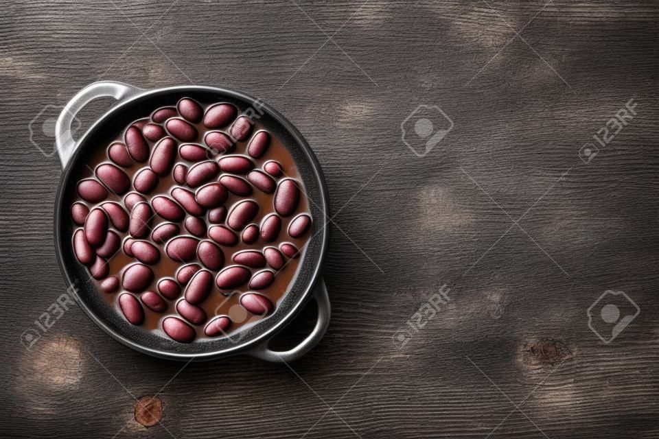 Comida enlatada de frijoles rojos, sobre fondo de mesa de madera oscura antigua, vista superior plana con espacio de copia para texto