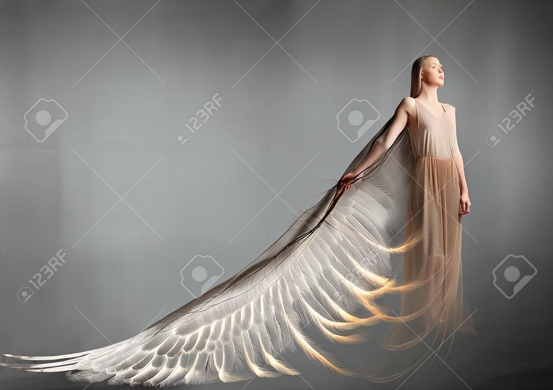 Attractive woman with angel wings on concrete background