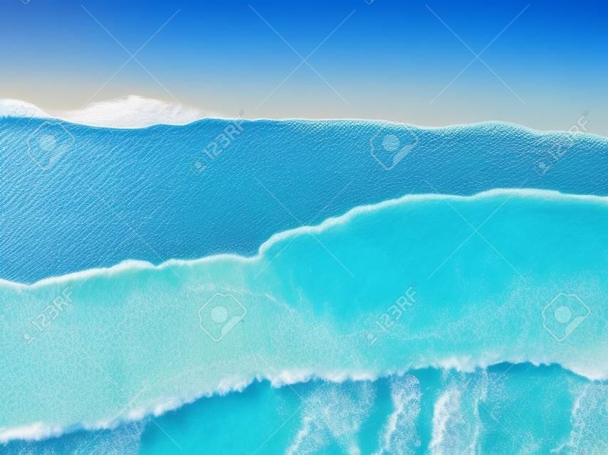 Vue aérienne de haut en bas sur la plage de l'océan avec de l'eau bleue, des vagues avec de la mousse et des embruns et du sable fin, belle destination de vacances d'été