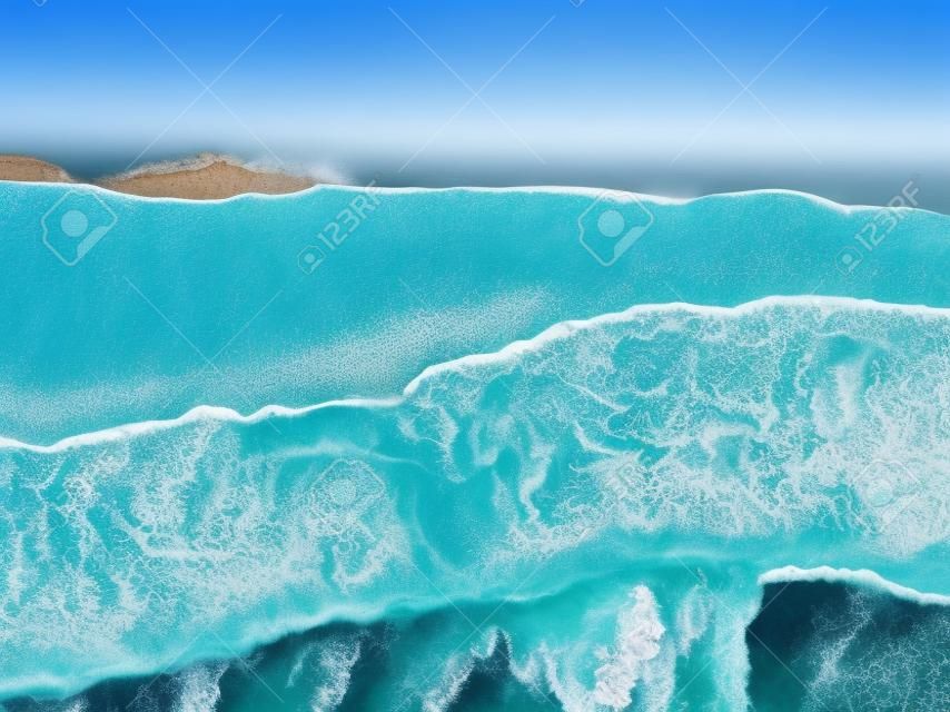 Ocean beach aerial top down view with blue water, waves with foam and spray and fine sand, beautiful summer vacation holidays destination