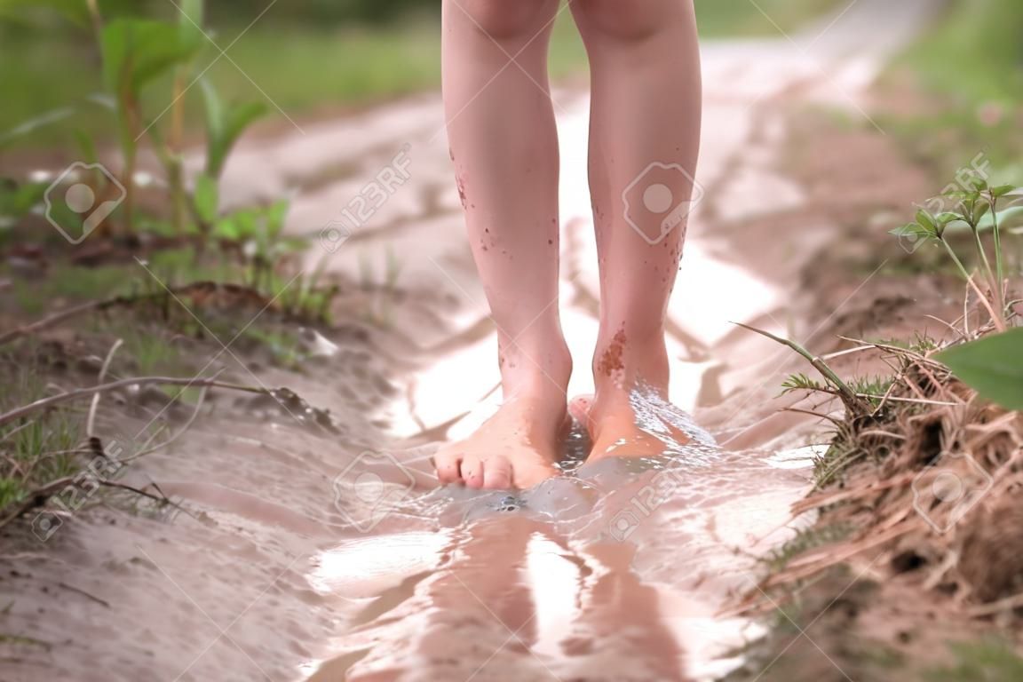 Barfüßiges Mädchen geht nach dem Sommerregen auf dem Land durch eine Wasserpfütze.