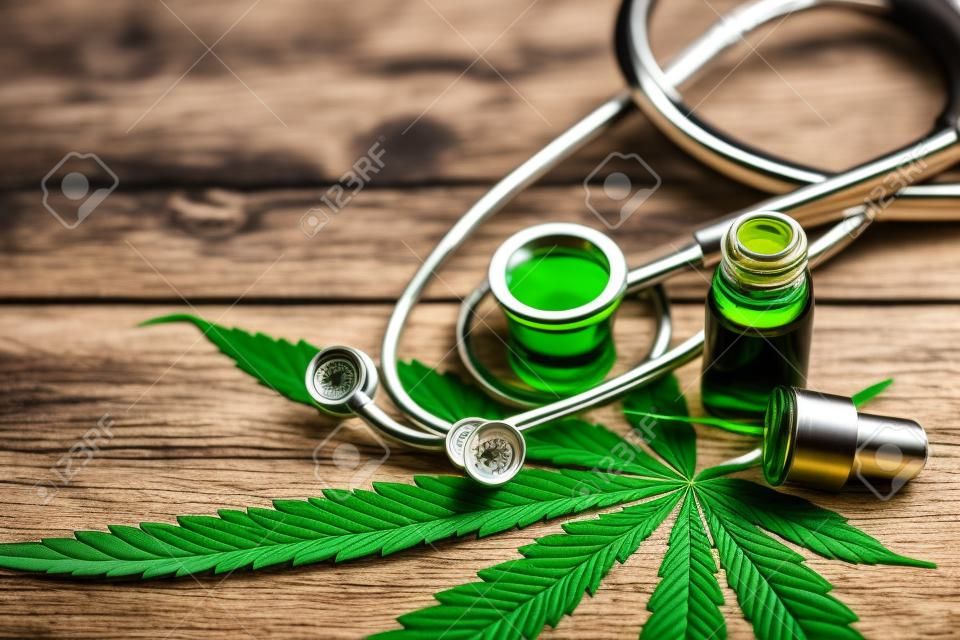 Ekstrakt z olejku konopnego z konopi indyjskich z zielonym liściem marihuany i stetoskopem medycznym wyizolowanym na tle starego stołu z drewna.