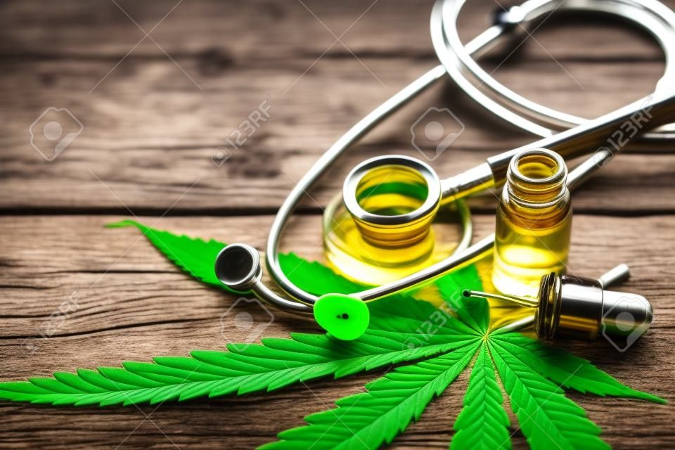 Extracto de aceite esencial de cáñamo de cannabis con hoja verde de marihuana y estetoscopio médico aislado en el fondo de la mesa de madera vieja.