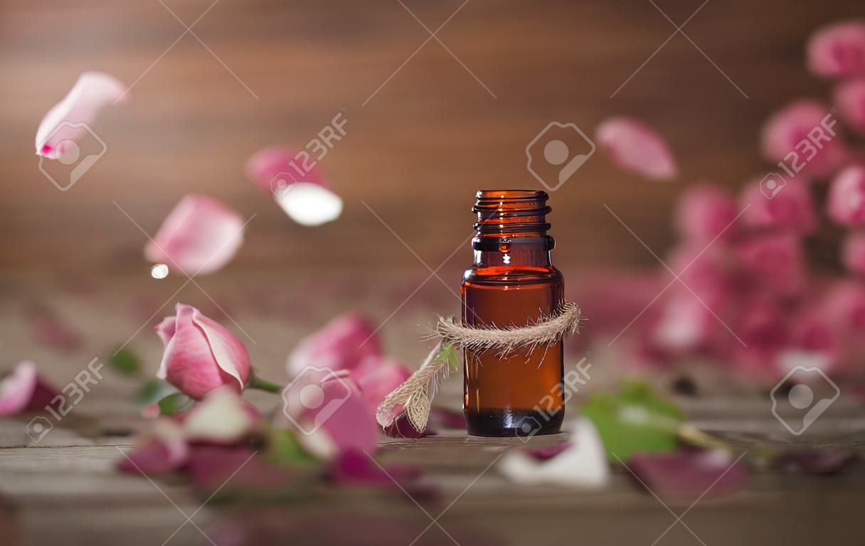 Closeup de garrafa com óleo essencial de rosa com folhas caindo no fundo de madeira.