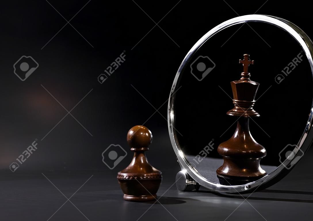 Pawn looking in the mirror and seeing a king. Black background.
