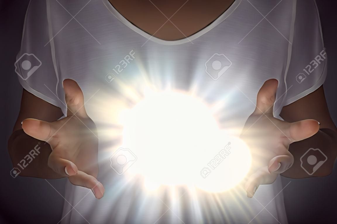 Fenômeno de energia de cura - fêmea em túnica branca com as mãos separadas no peito com uma luz orbe branca brilhante entre