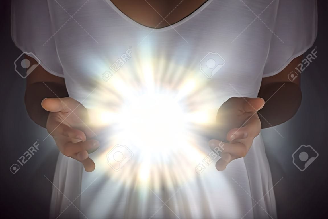 Fenômeno de energia de cura - fêmea em túnica branca com as mãos separadas no peito com uma luz orbe branca brilhante entre