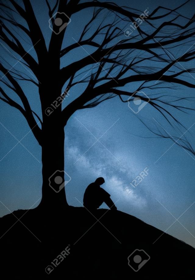 sziluettje egy ember ül egy fa alatt