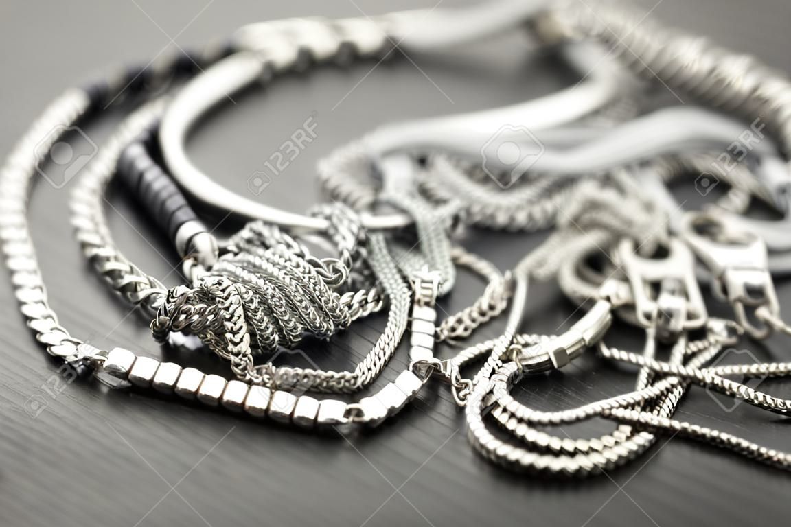 Pila de cadenas de plata surtidos con cadenas caja brillantes, cadenas de cubo y cadena de eslabones ordinaria sobre un fondo gris conceptual de bisutería