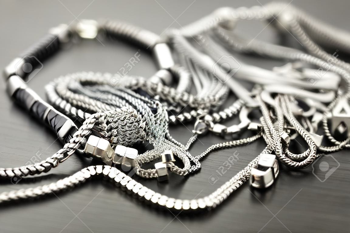Pila de cadenas de plata surtidos con cadenas caja brillantes, cadenas de cubo y cadena de eslabones ordinaria sobre un fondo gris conceptual de bisutería