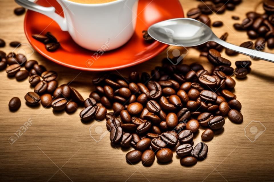 Coup of coffe alongside with coffe beans on wooden table alongside with spoon
