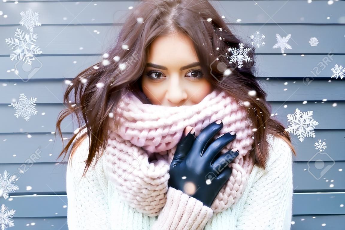 Winterportret van jonge mooie brunette vrouw met gebreide snood bedekt met sneeuw. Sneeuwende winter schoonheid mode concept.