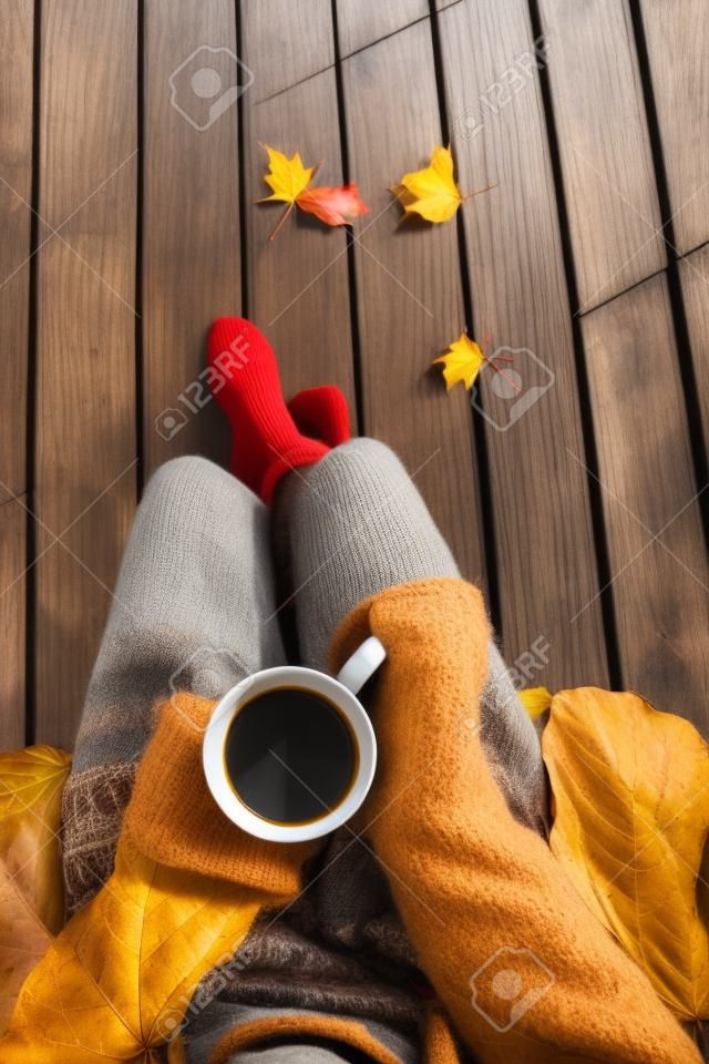 Primo piano vista dall'alto della donna in possesso di una tazza di caffè. ponte patio in legno con foglie cadono come sfondo