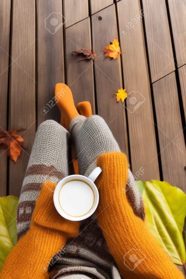 Primo piano vista dall'alto della donna in possesso di una tazza di caffè. ponte patio in legno con foglie cadono come sfondo