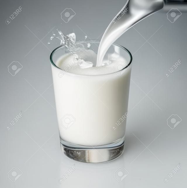 Latte fresco versando in un bicchiere schizzo, isolato su bianco