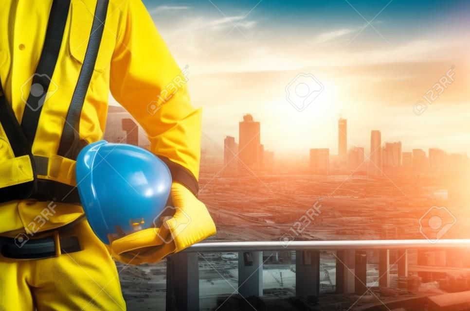 Engineer holding a yellow helmet with a backdrop of the city and industry.