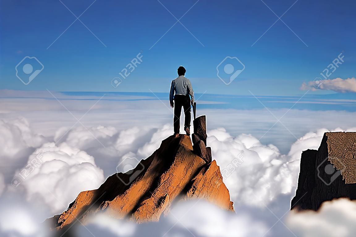 Koncepcja sukcesu, biznesmen stojący na szczycie klifu górskiego nad chmurami i patrząc w przyszłość, koncepcja konkurencji i lidera.