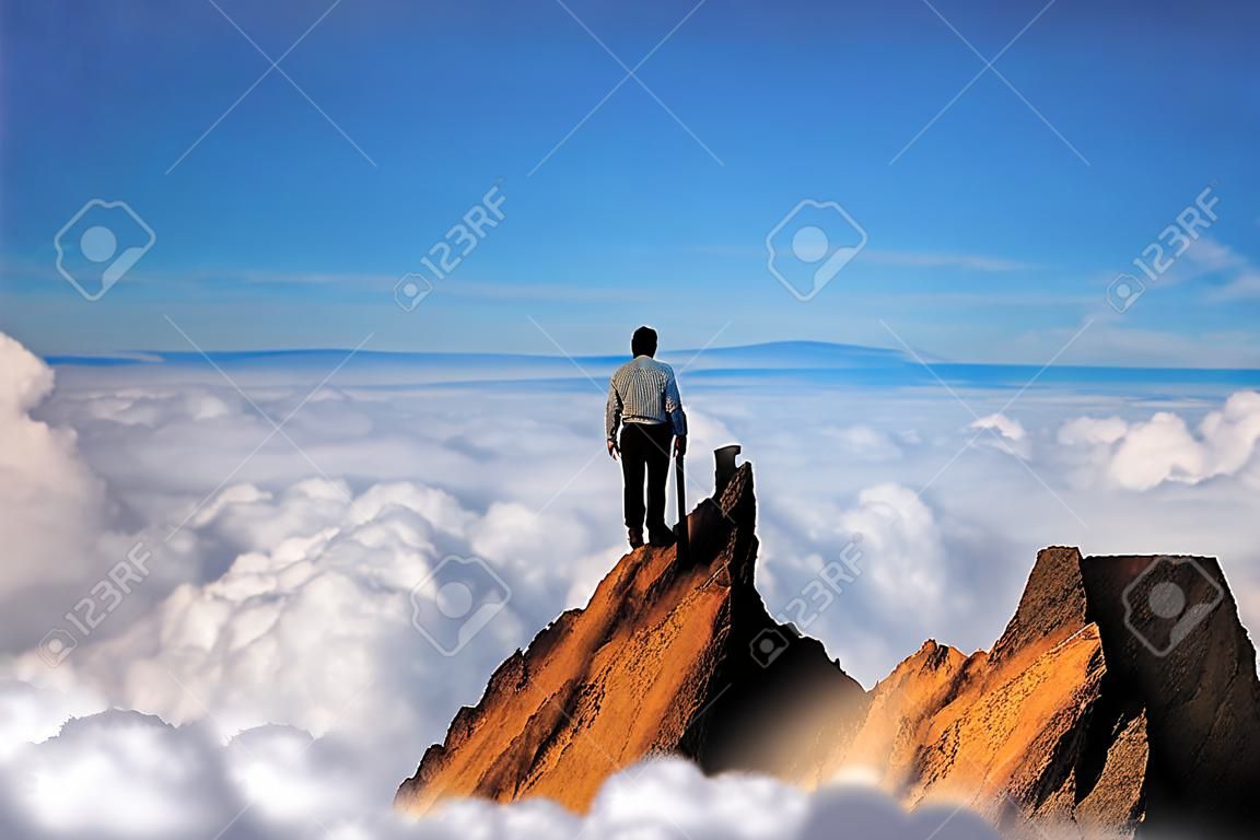 Erfolgskonzept, Geschäftsmann, der auf der Spitze der Bergklippe über den Wolken steht und nach vorne schaut, Wettbewerb und Führungskonzept.