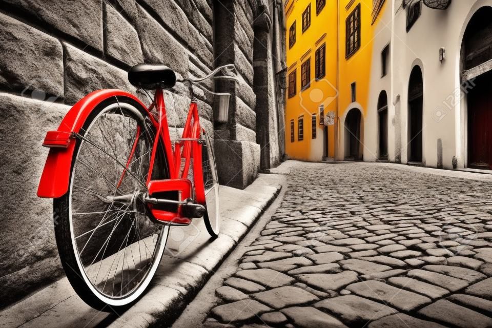 Retro vintage red bike on cobblestone street in the old town. Color in black and white. Old charming bicycle concept.