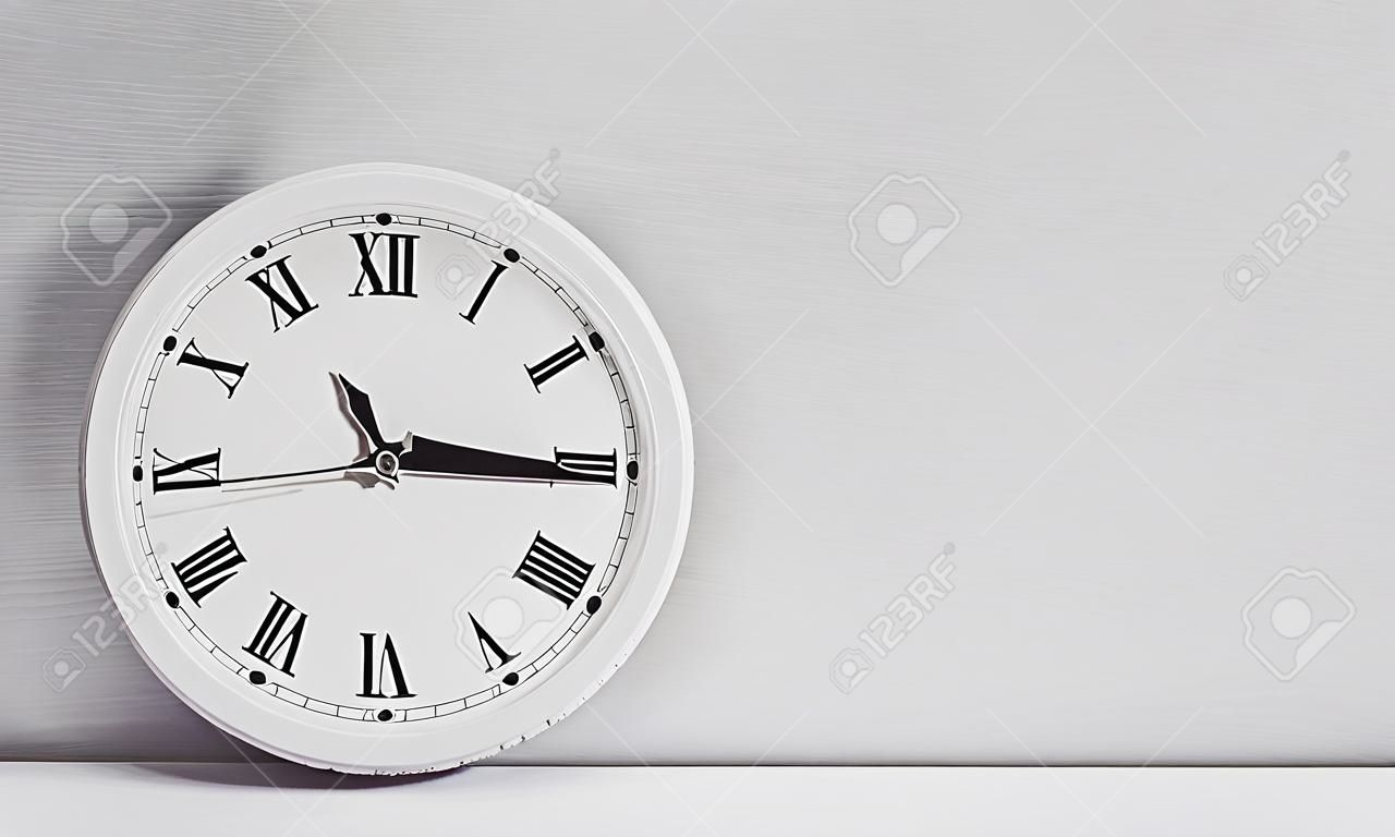 L'orologio bianco del primo piano per decorare mostra un quarto alle quattro o 3:45 pm sullo scrittorio di legno bianco e fondo strutturato della carta da parati nel tono in bianco e nero con lo spazio della copia