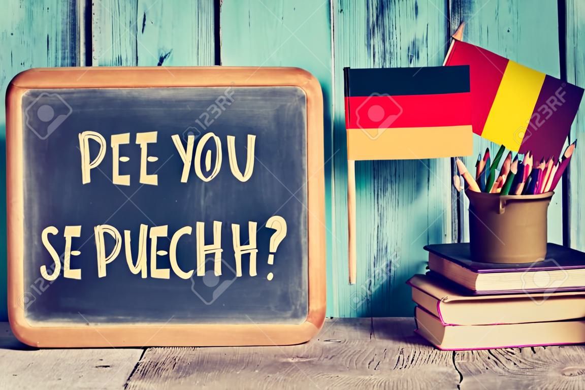 um quadro-negro com a pergunta sprechen sie deutsch? você fala alemão? escrito em alemão, um pote com lápis, alguns livros e a bandeira da Alemanha, em uma mesa de madeira