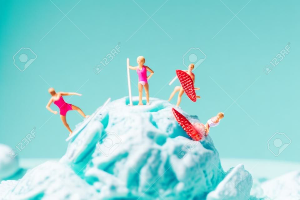 Libre de certaines personnes miniatures en maillot de bain surfant sur une boule de crème glacée à la fraise, sur un fond bleu avec un espace vide