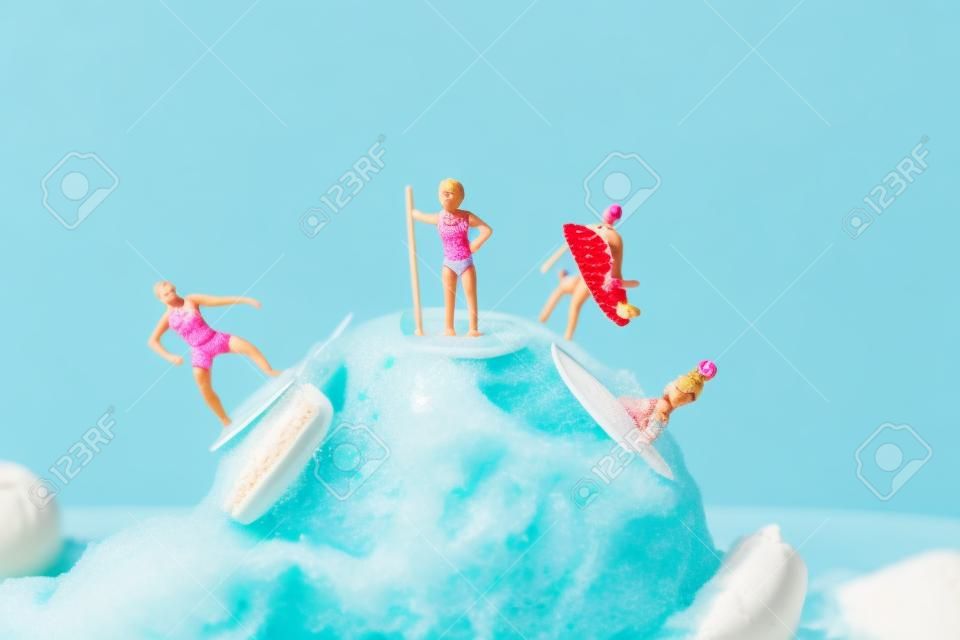primo piano di alcune persone in miniatura in costume da bagno che navigano su una palla di gelato alla fragola, su uno sfondo blu con un po' di spazio vuoto