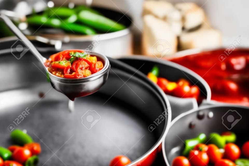 closeup de uma panela com molho de tomate e algumas frigideiras com tomates cozidos cereja e pimentas verdes, em uma cozinha profissional