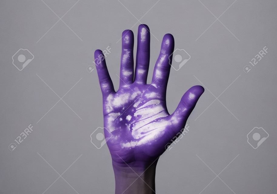 closeup of the raised hand of a man with some stains of purple paint in his palm, on a pale gray background