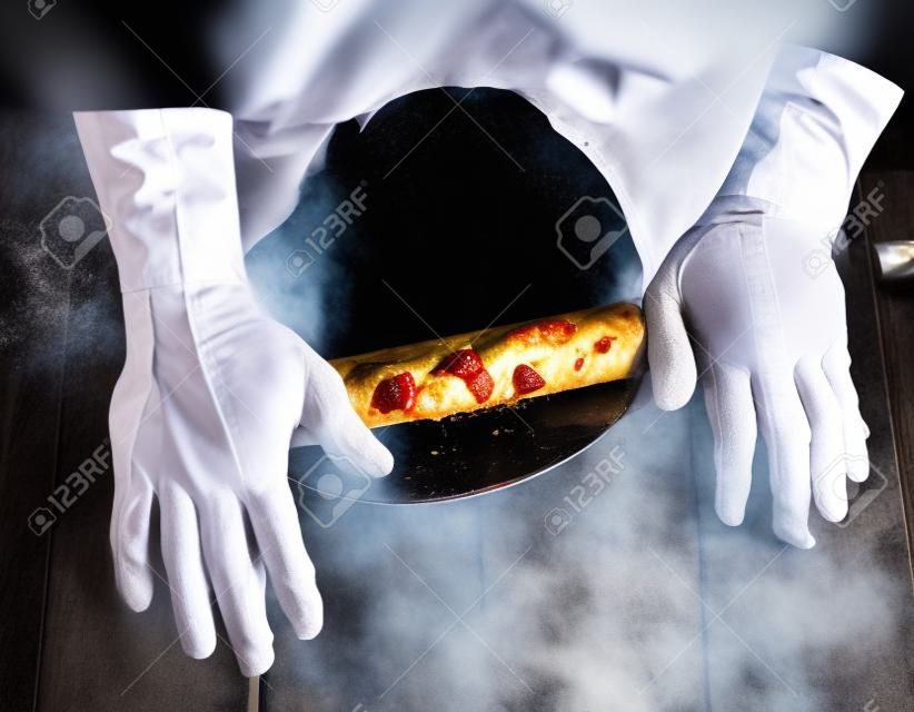 le chef en tunique noire roule une pâte pour une pizza ronde, vue de dessus