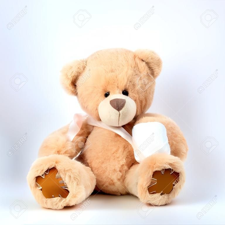grande urso de pelúcia bege com patches senta-se em um fundo branco, a pata esquerda é enfaixada com uma bandagem médica branca, conceito de pediatria, tratamento de animais