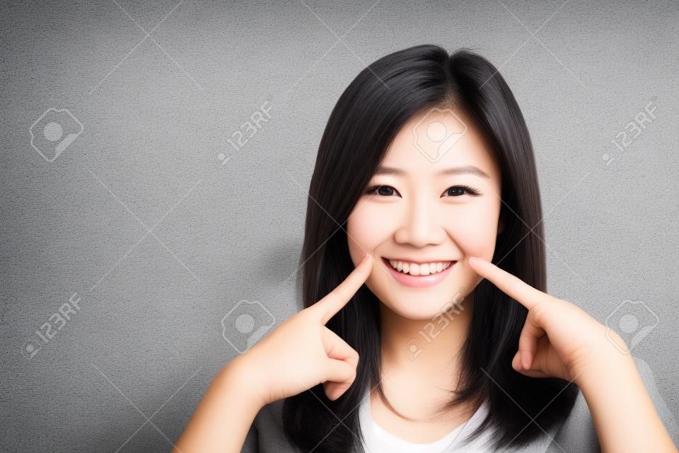 Portret pięknej młodej azjatyckiej kobiety szczęścia stojącego palcem dotknąć policzka na szarym tle cementu tekstury grunge ściany z cegły, bizneswoman jest uśmiechnięta na betonie, koncepcja ludzi biznesu.