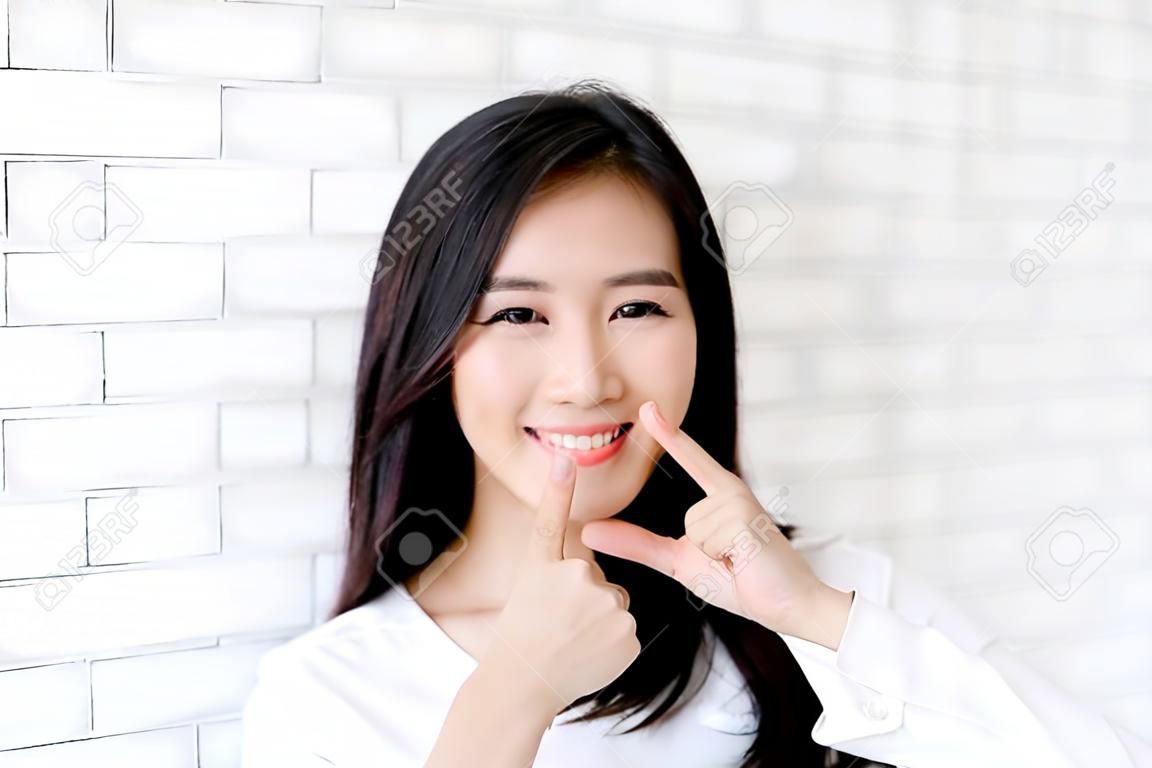 グレーのセメントテクスチャグランジ壁レンガの背景に指タッチ頬に立っている美しい若いアジアの女性の幸せの肖像画は、ビジネスウーマンは、コンクリート、ビジネスマンのコンセプトに笑顔です。