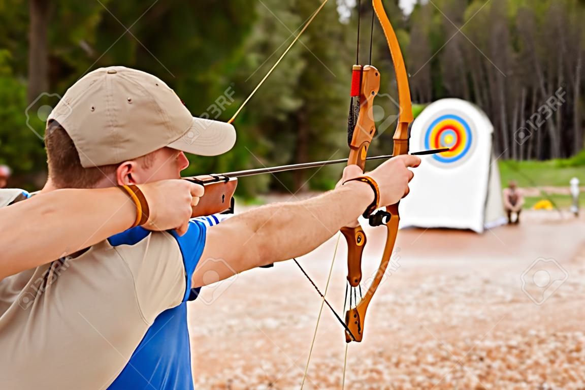homem jovem fazendo tiro com arco, visando o alvo, divertido conceito de atividade ao ar livre